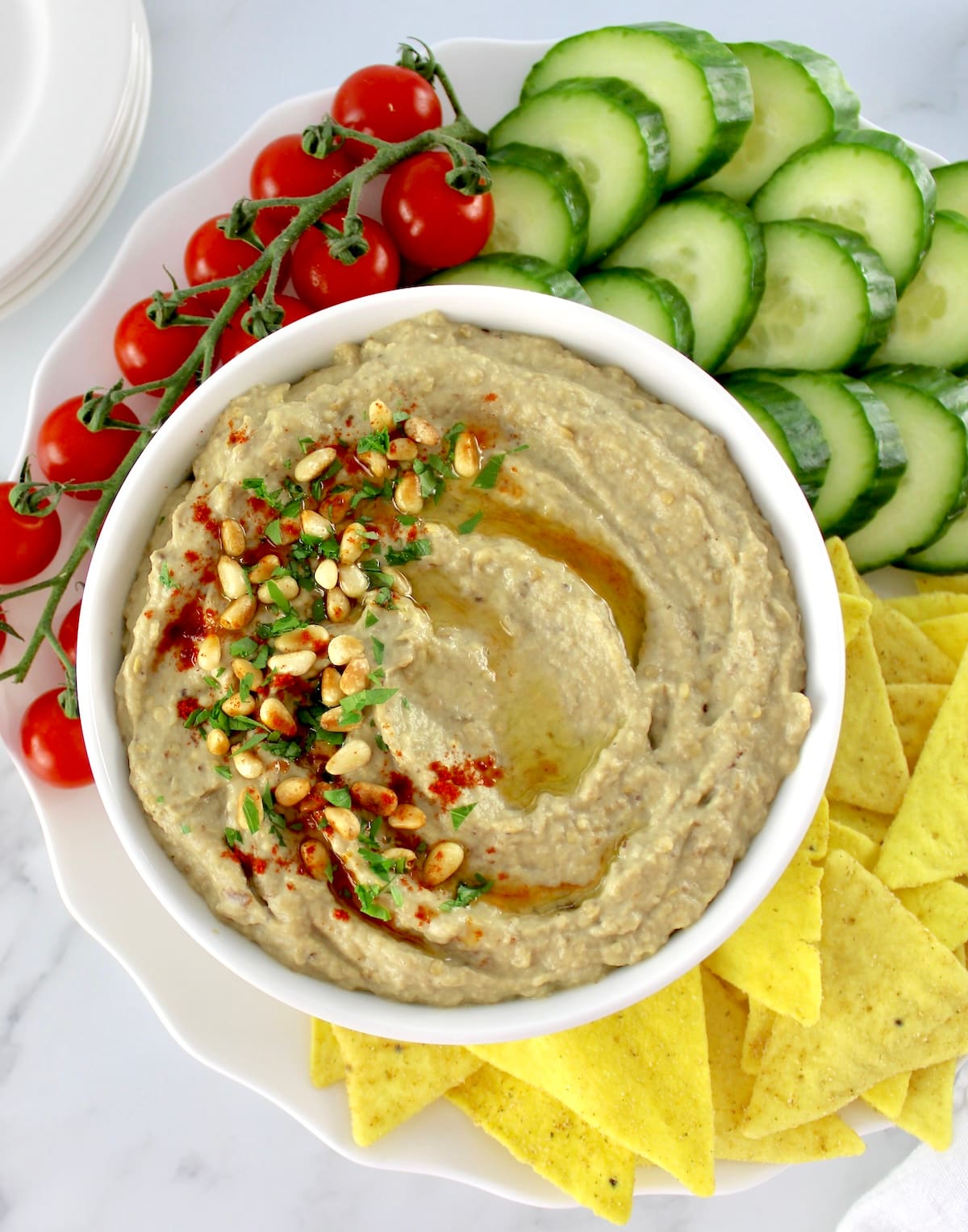 overhead view of Baba Ganoush in white bowl with tortilla chips, cucumber slices and cherry tomatoes on side