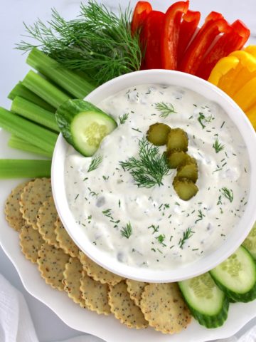 Dill Pickle Dip in white bowl with raw veggies and crackers around