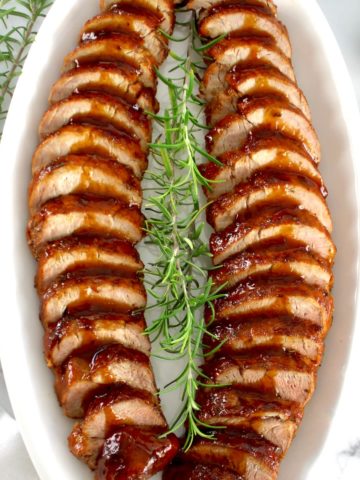 Honey Glazed Pork Tenderloin sliced on a white oval platter with fresh rosemary
