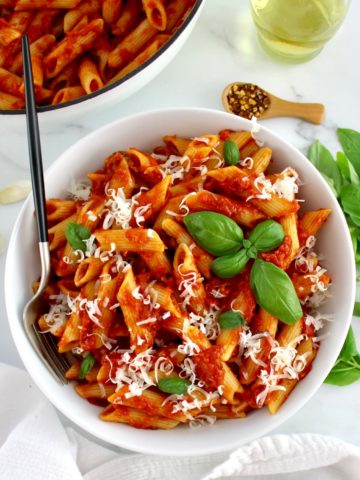 Penne Arrabbiata in white bowl with fork and white skillet in back
