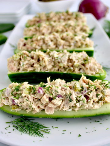 Dill Pickle Tuna Cucumber Boats lined up on white plate with fresh dill